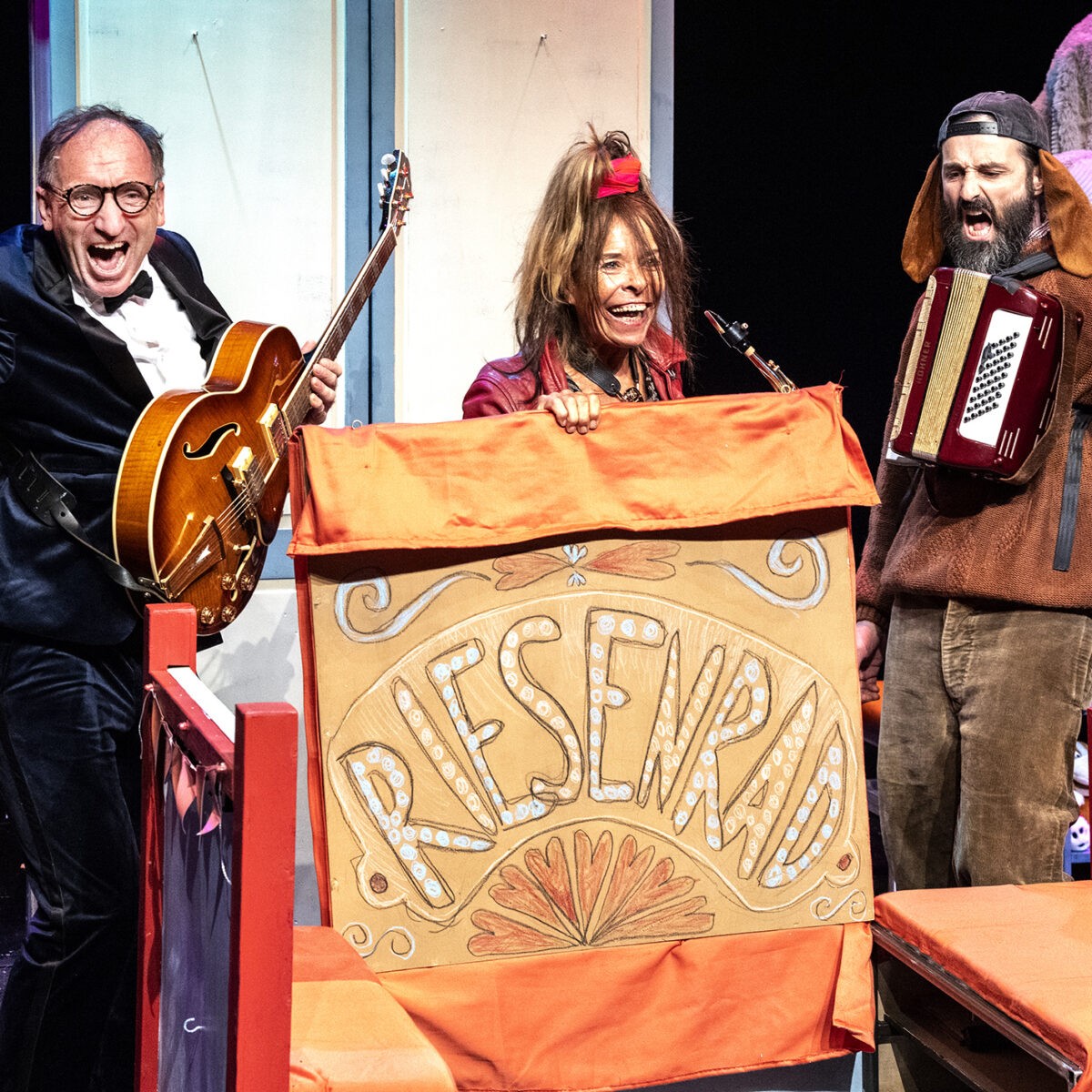 Drei Menschen jubeln. Zwei tragen Musikinstrumente, eine hält ein Schild mit der Aufschrift "Riesenrad"